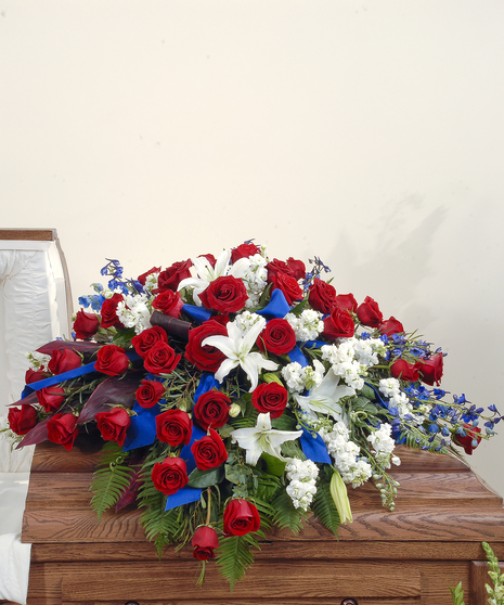 A large casket spray of roses, lilies, stock, and delphinium, mixed with greenery. Displayed on top of a closed casket.