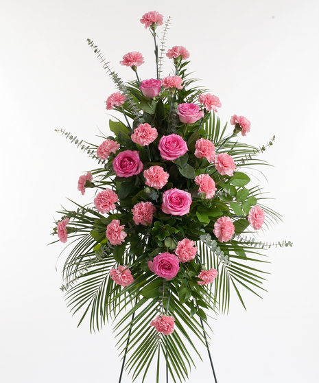 A large spray of roses and carnations, mixed with greenery. Displayed on a white easel against a white background.