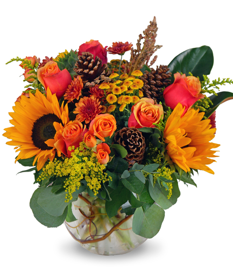  fresh flower arrangement in a glass bubble bowl featuring cherry brandy roses, spray roses, solidago, magnolia, eucalyptus, and pinecones, for a seasonal sympathy tribute.