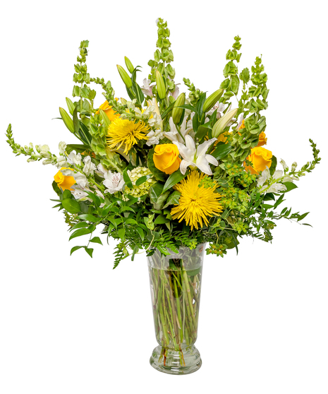 A large floral arrangement with white lilies, yellow roses, hydrangeas, and spider mums, accented by greenery, displayed in a clear glass vase against a white background.